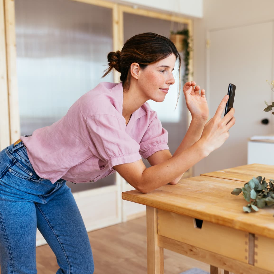 Woman leaning over a table looking at her phone